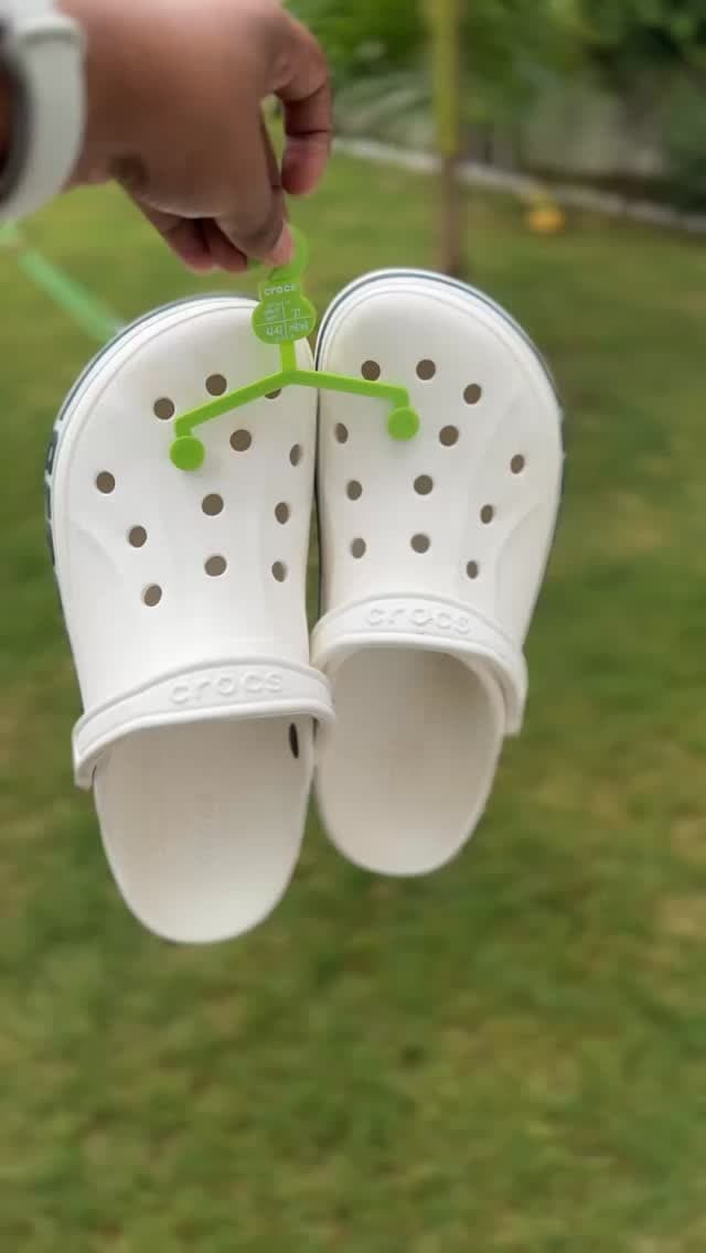 A pair of white Crocs decorated with charms, held up outdoors