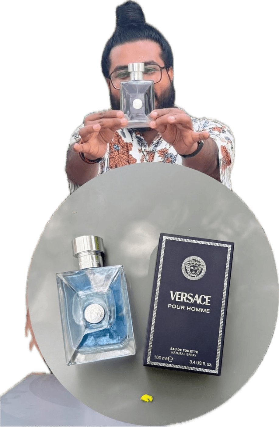Akio holding a bottle of Versace Pour Homme in front of palm fronds, with the bottle and box shown below